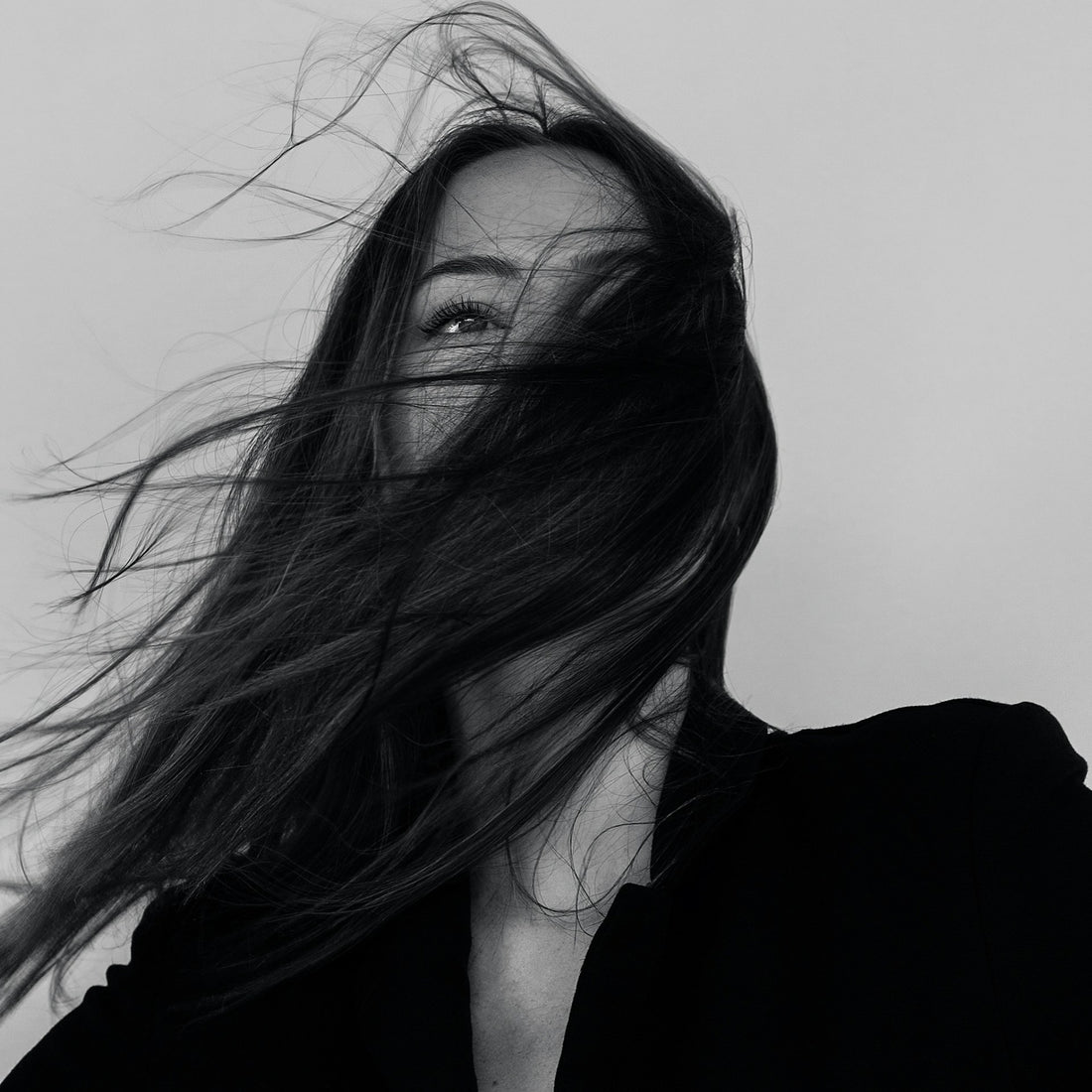 Black and white portrait of a woman with windswept hair, symbolizing natural beauty and strength. Perfect visual for winter hair care tips and MOY's wellness products designed to restore hair health and radiance.